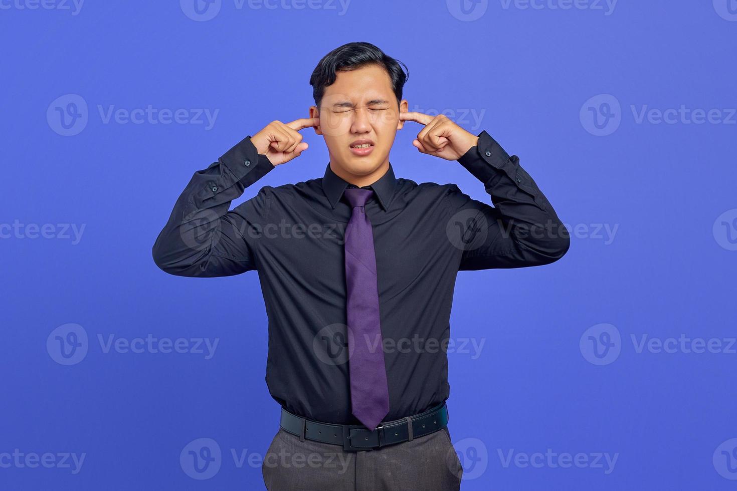 gefrustreerde jonge knappe zakenman die oor bedekt met woedeuitdrukking op paarse achtergrond foto