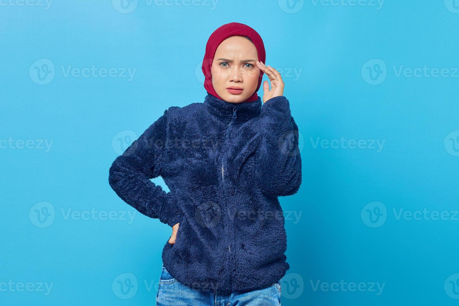 gefrustreerde jonge Aziatische vrouw met gezicht met een hand op blauwe achtergrond foto