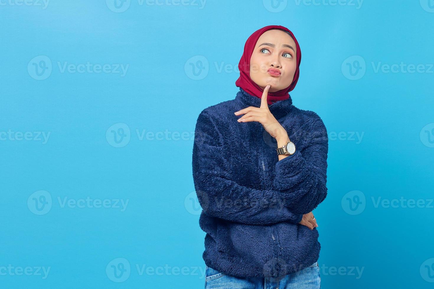 peinzende jonge aziatische vrouw die aan iets op blauwe achtergrond denkt foto