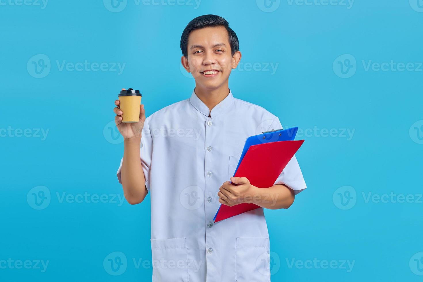 glimlachende jonge aziatische man verpleegster met map en koffie over blauwe achtergrond foto