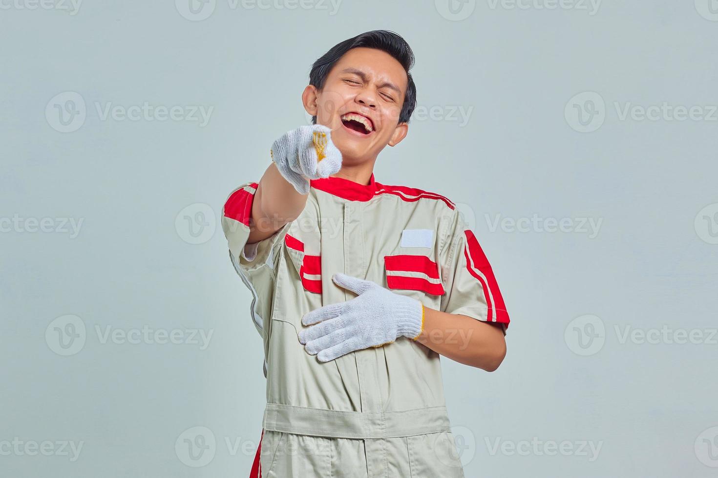 portret van een knappe man met een mechanisch uniform met luid gelach met de hand op de buik en een wijzende vinger naar de camera foto