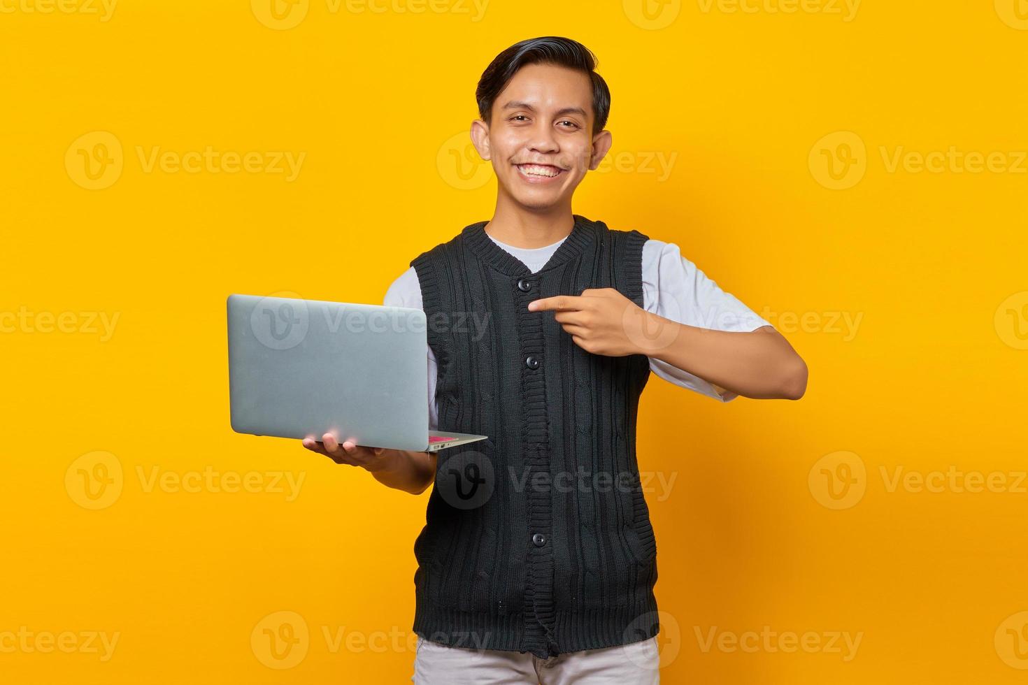 lachende knappe jonge man wijzende vinger naar laptop op gele achtergrond foto