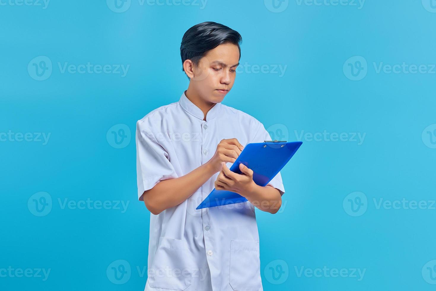 glimlachende jonge verpleger die aantekeningen maakt op klembord op blauwe achtergrond foto
