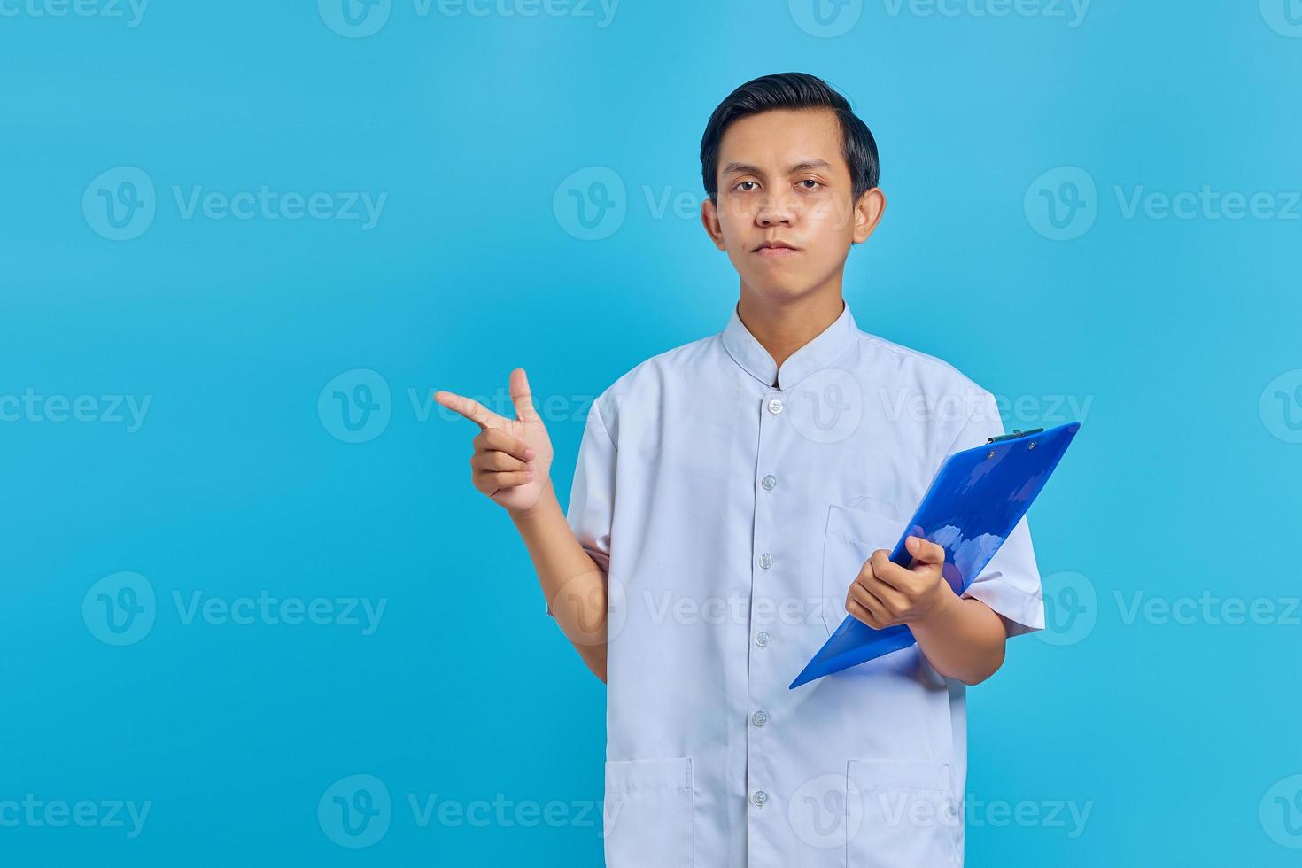 portret van glimlachende verpleger die klembord vasthoudt en zijwaarts wijst op een blauwe achtergrond foto