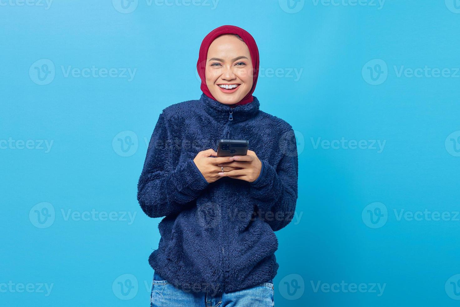 portret van lachende jonge Aziatische vrouw met behulp van een mobiele telefoon op blauwe achtergrond foto