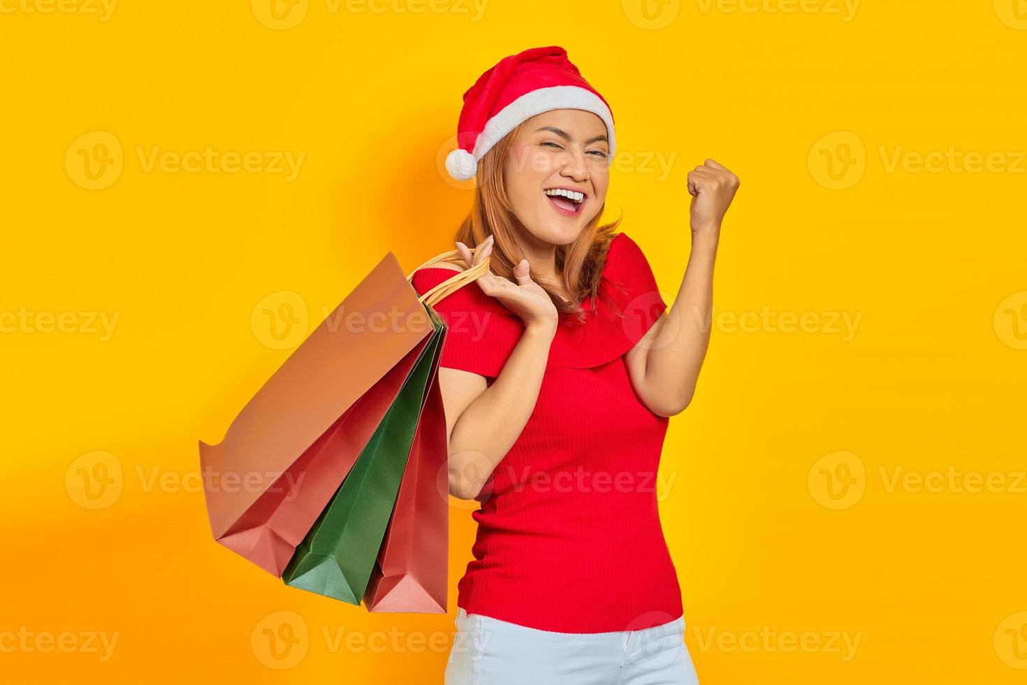 vrolijke jonge vrouw met kerstmuts die boodschappentassen vasthoudt en winkeltevredenheid viert foto
