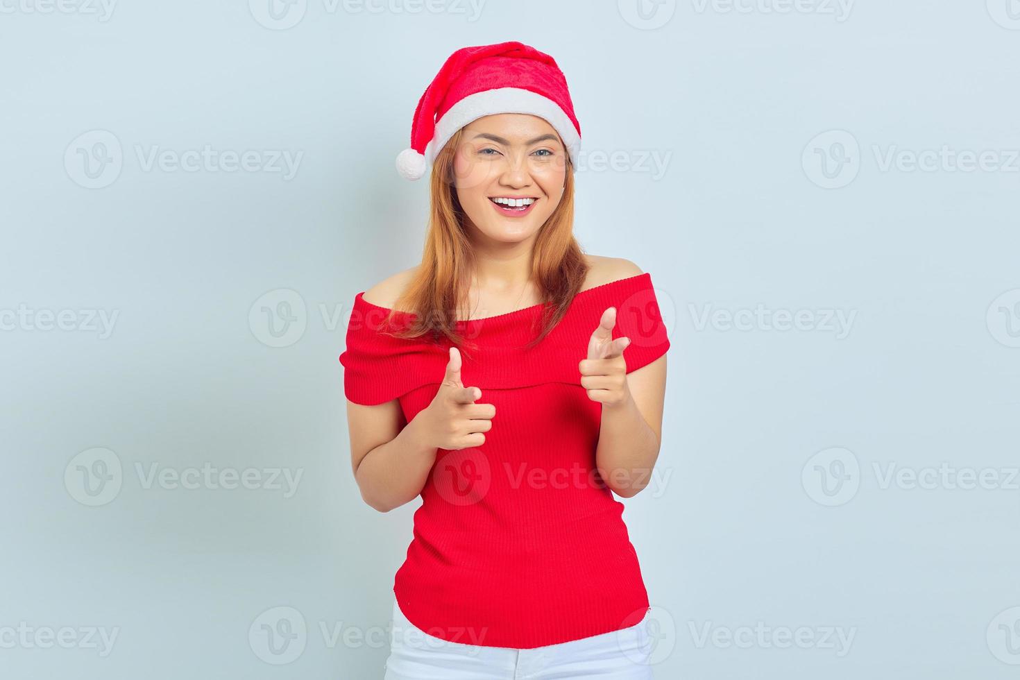 verticaal, van, het glimlachen, jonge, aziatische vrouw, vervelend, rode jurk, en, kerstmuts, wijzende, vingertje, op, camera, geïsoleerde, op wit, background foto