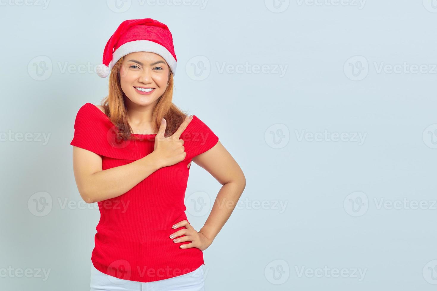 portret van glimlachende jonge aziatische vrouw die met vinger op witte achtergrond wijst om ruimte te kopiëren foto