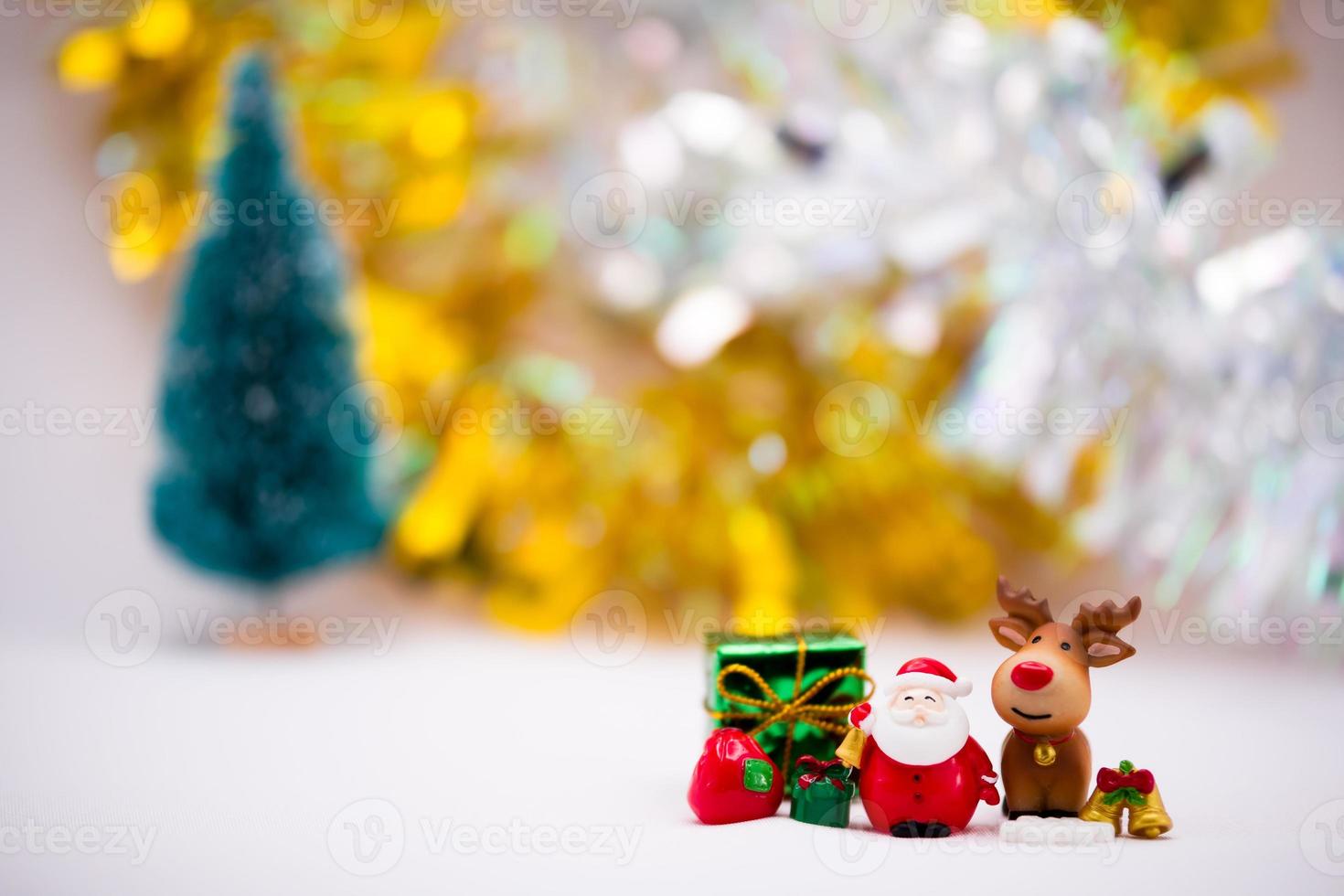 Kerstman en rendieren beeldjes gemaakt van keramiek of hars op zachte witte achtergrond. gouden en zilveren achtergrond met wazig kerstboom. groene geschenkdoos en gouden bel. foto