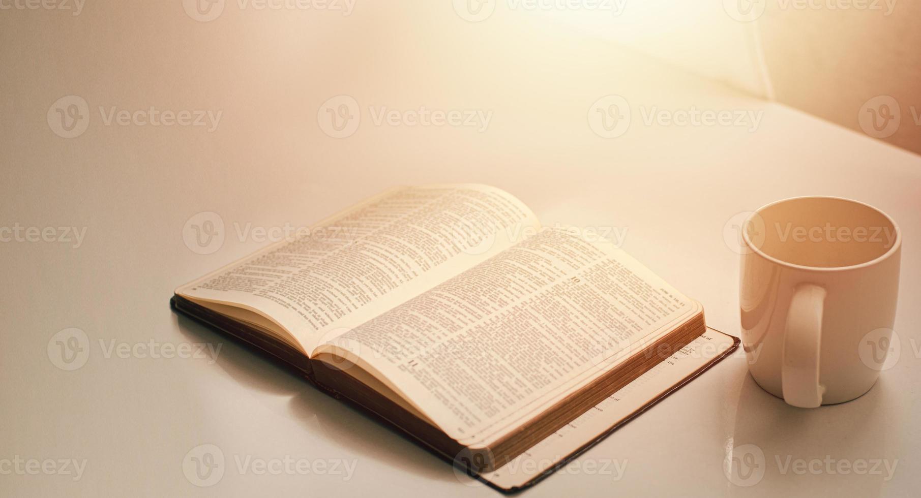 open een bijbel bij het raam met een kopje koffie voor het ochtendlicht. en zet het op een houten tafel met een raamlicht foto