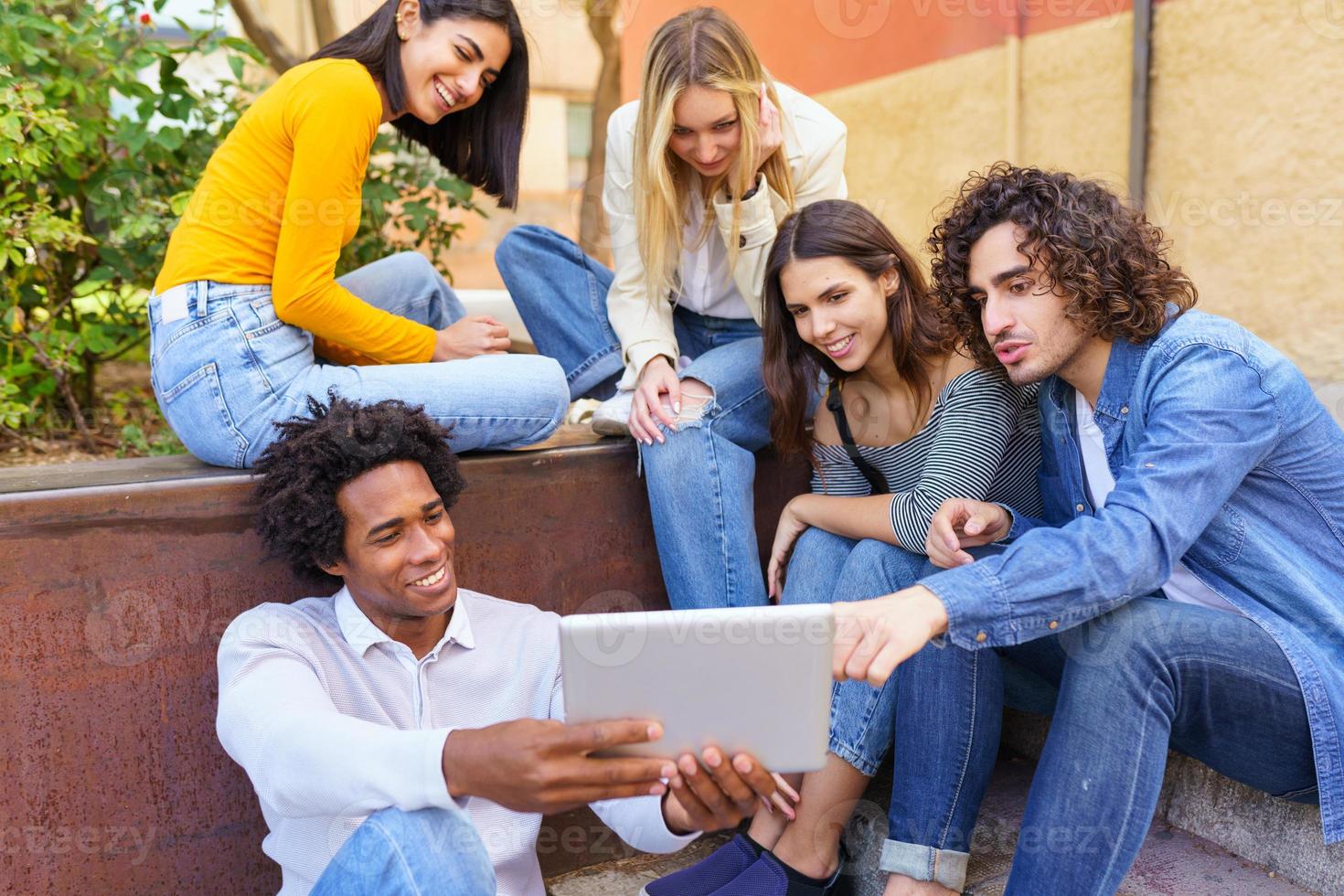 multi-etnische groep jonge mensen die buiten op stedelijke achtergrond naar een digitale tablet kijken. foto