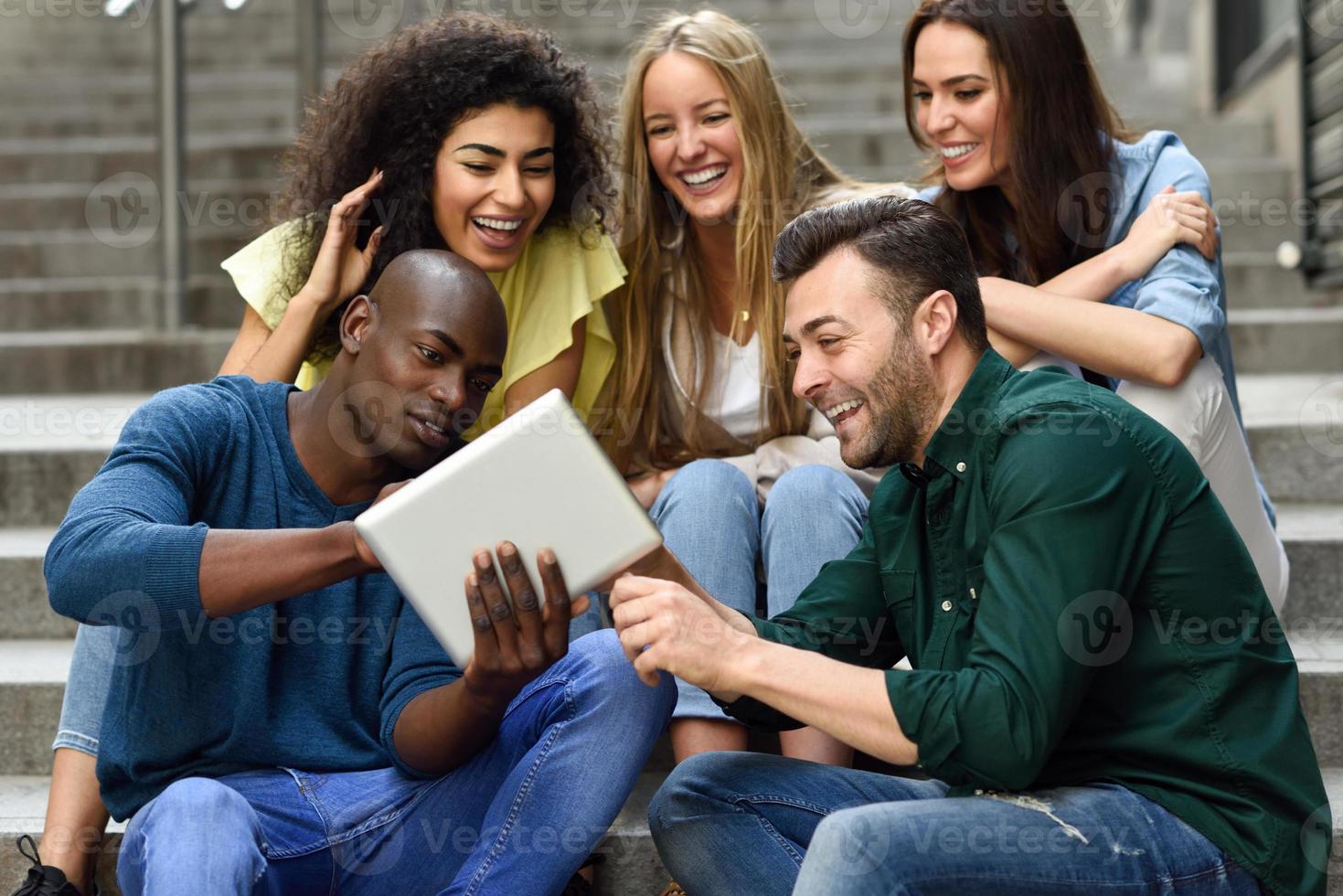 multi-etnische groep jongeren die naar een tabletcomputer kijken foto