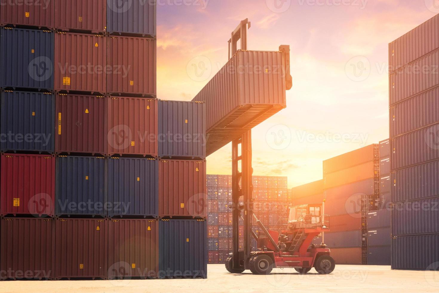 vorkheftruck die vrachtcontainer in scheepvaartwerf of dokwerf opheft tegen zonsopganghemel met vrachtcontainerstapel op achtergrond voor transportimport, -export en logistiek industrieel concept foto