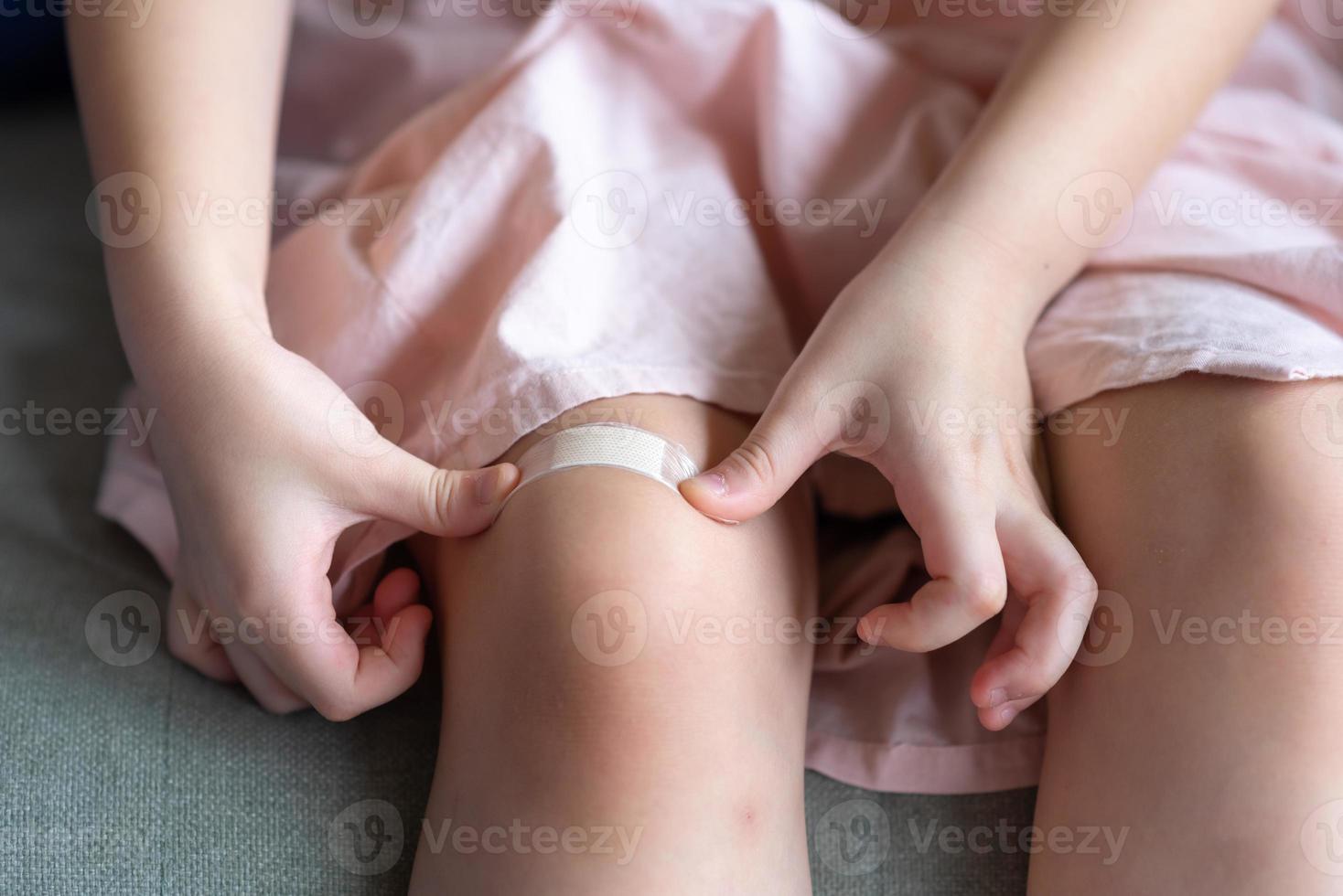 close-up van kinderen die thuis gipspleister op haar knie leggen foto