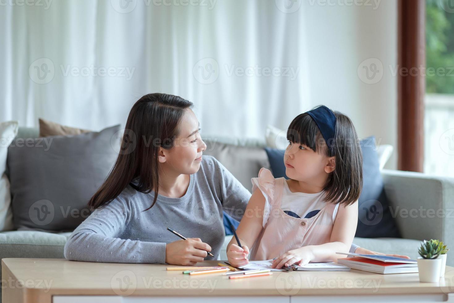 Aziatische moeder leert haar schattige dochtertje om thuis in de woonkamer te studeren foto