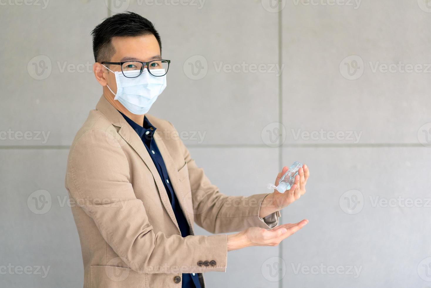 zakenman die een masker draagt en persoonlijk ontsmettingsmiddel gebruikt om zijn hand op kantoor schoon te maken om de hygiëne te behouden. preventief tijdens de periode van epidemie van coronavirus of covid19. foto