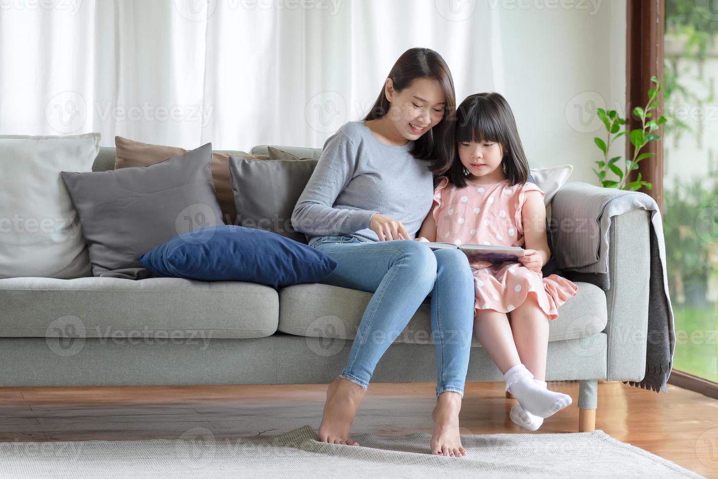 gelukkige Aziatische moeder die haar schattige dochter leert om thuis in de woonkamer te studeren foto