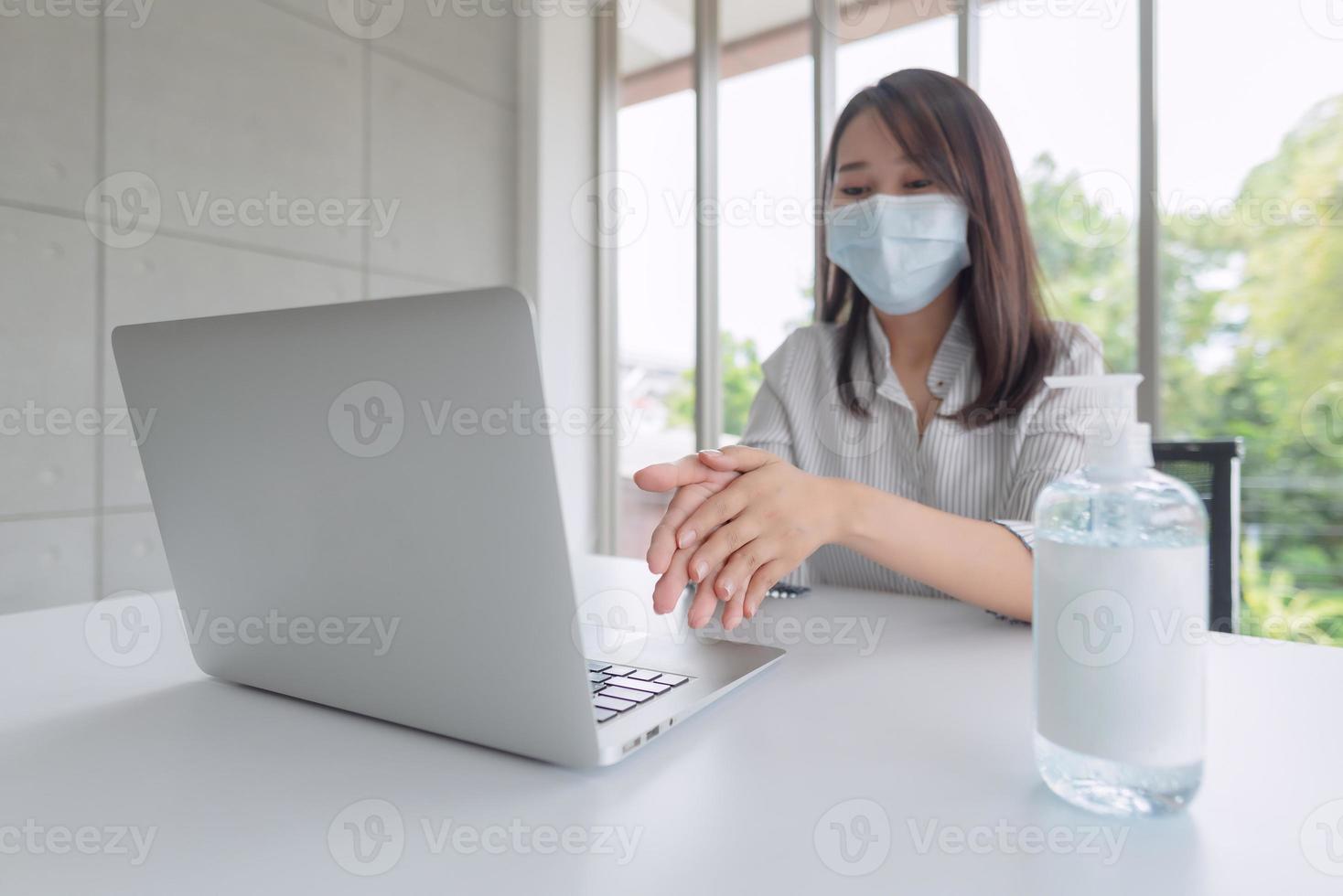 zakenvrouw die een masker draagt en persoonlijk ontsmettingsmiddel gebruikt om haar hand op kantoor schoon te maken om de hygiëne te behouden. preventief tijdens de periode van epidemie van coronavirus of covid19. foto