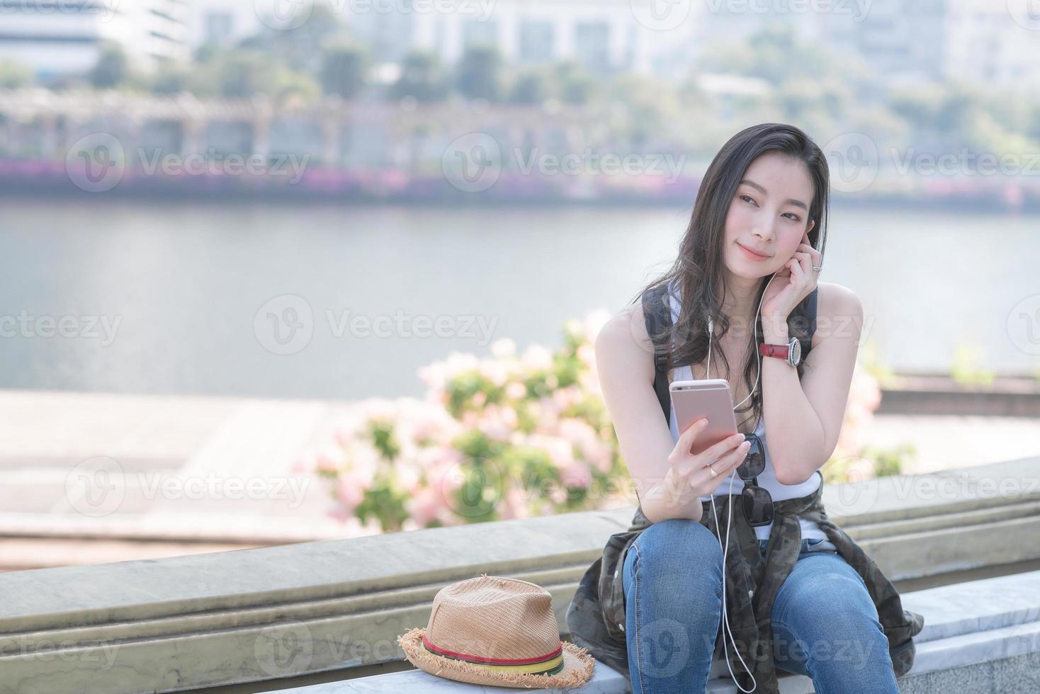 mooie Aziatische solo-toeristische vrouw die ontspant en geniet van het luisteren naar de muziek op een smartphone in het centrum van de stad. vakantie reizen in de zomer. foto