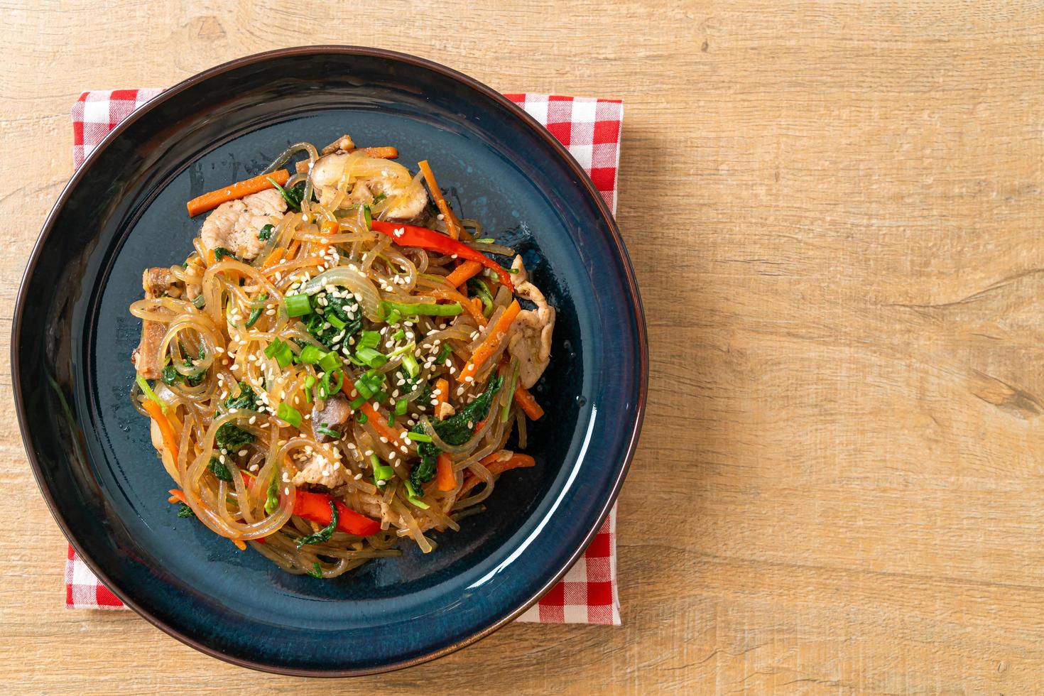 japchae of geroerbakte Koreaanse vermicelli noedels met groenten en varkensvlees gegarneerd met witte sesam foto