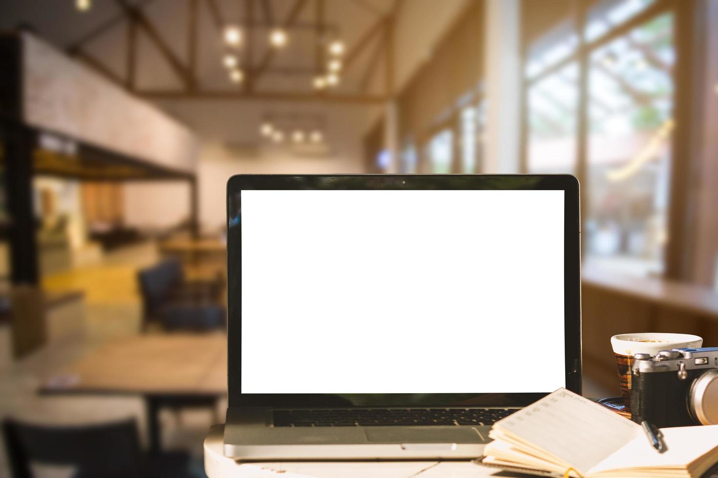 mockup afbeelding van laptop met leeg wit scherm met camera, notebook, koffiekopje op houten tafel van in de coffeeshop achtergrond. foto