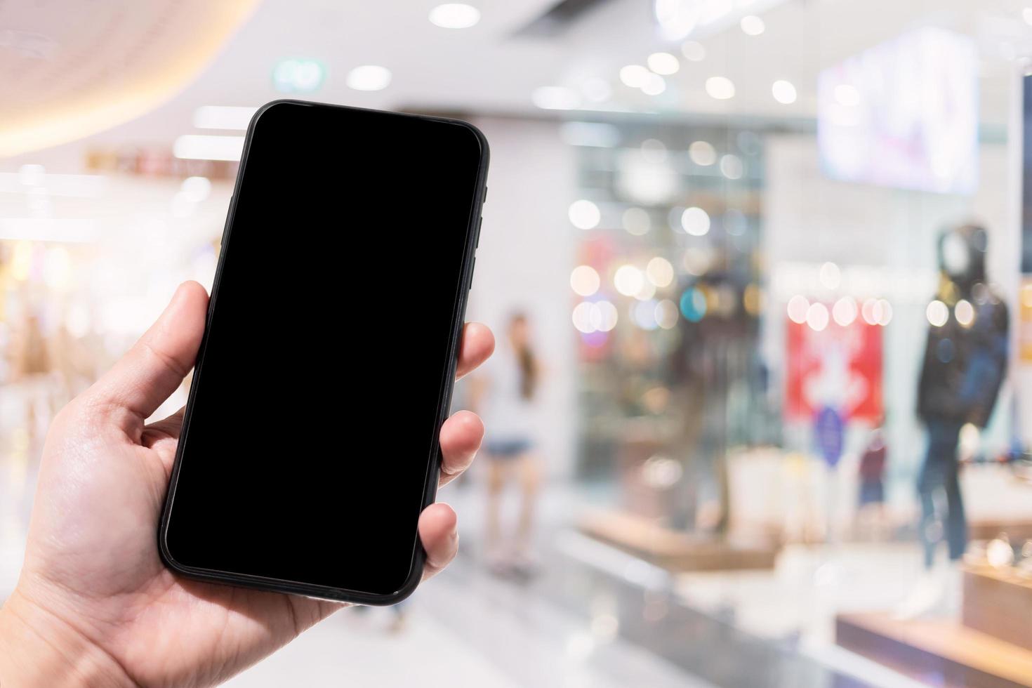 close-up van vrouwelijk gebruik smartphone wazig beelden in het winkelcentrum en kledingwinkel vervagen van de achtergrond. foto