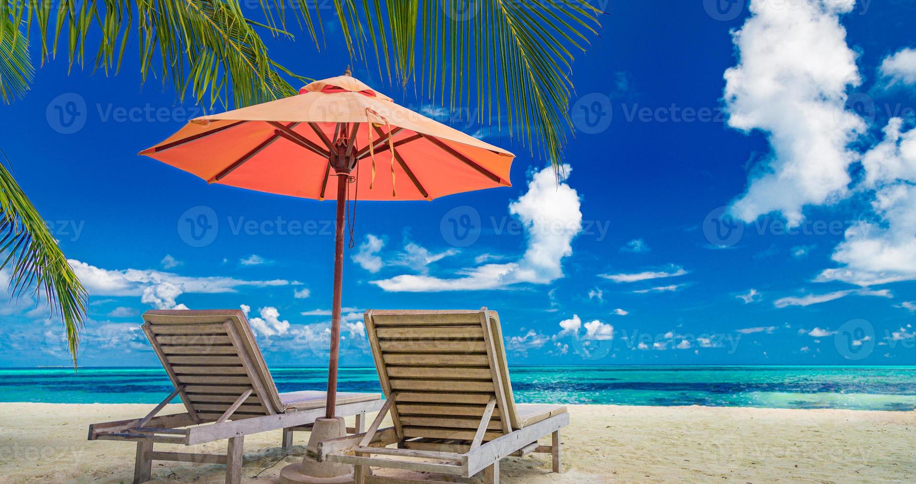 prachtig tropisch eilandlandschap, twee ligbedden, ligstoelen, parasol onder palmboom. wit zand, uitzicht op zee met horizon, idyllische blauwe lucht, rust en ontspanning. inspirerend strandresorthotel foto