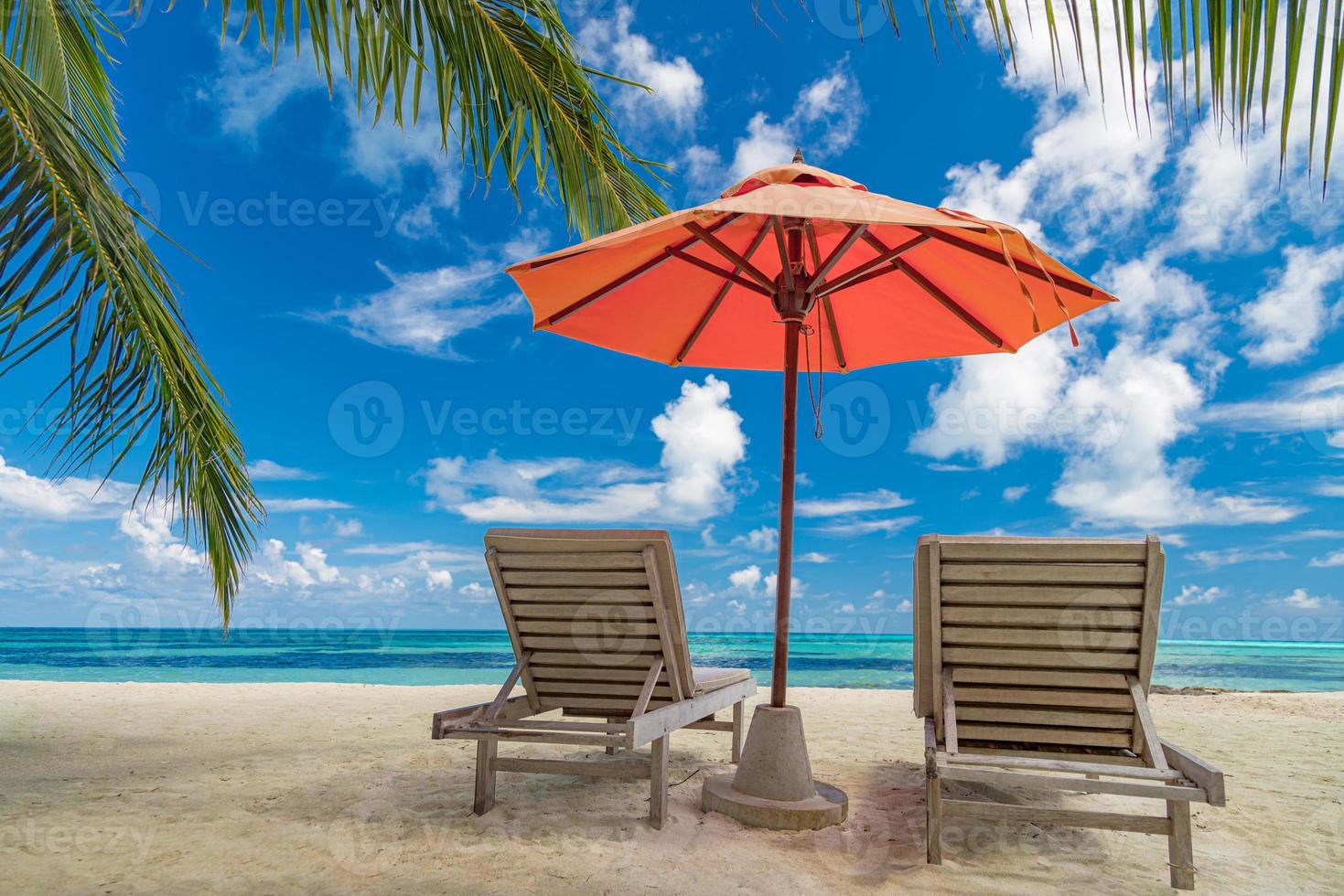 prachtig tropisch eilandlandschap, twee ligbedden, ligstoelen, parasol onder palmboom. wit zand, uitzicht op zee met horizon, idyllische blauwe lucht, rust en ontspanning. inspirerend strandresorthotel foto