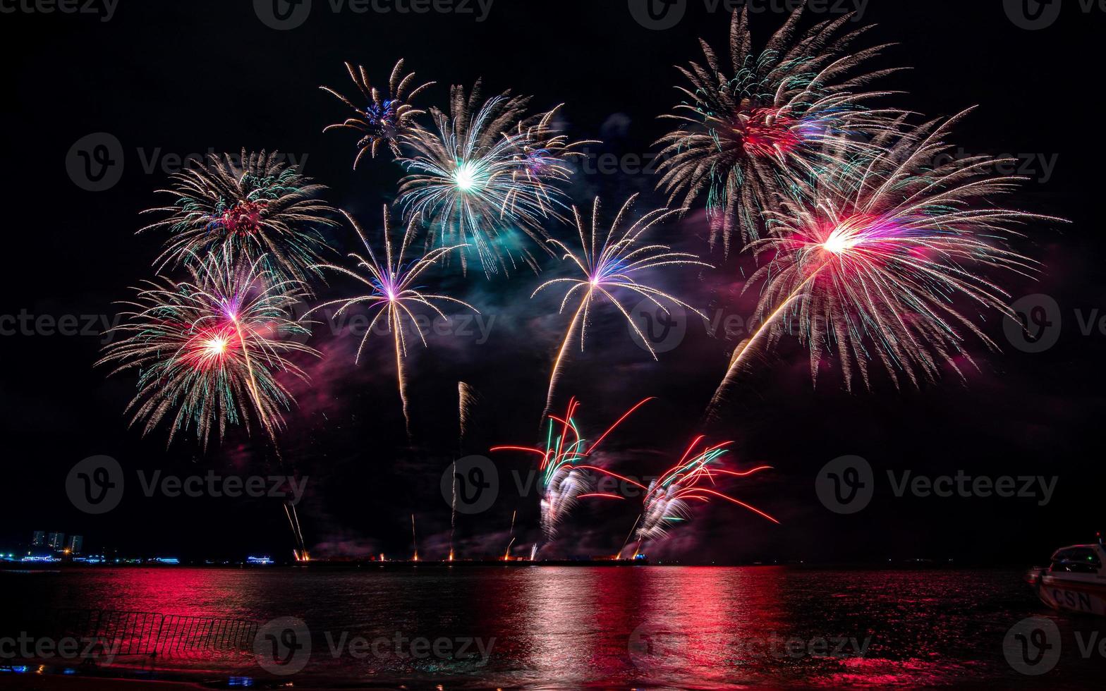 geweldig mooi kleurrijk vuurwerk op de feestavond, te zien op het zeestrand met veelkleurige reflectie op water foto