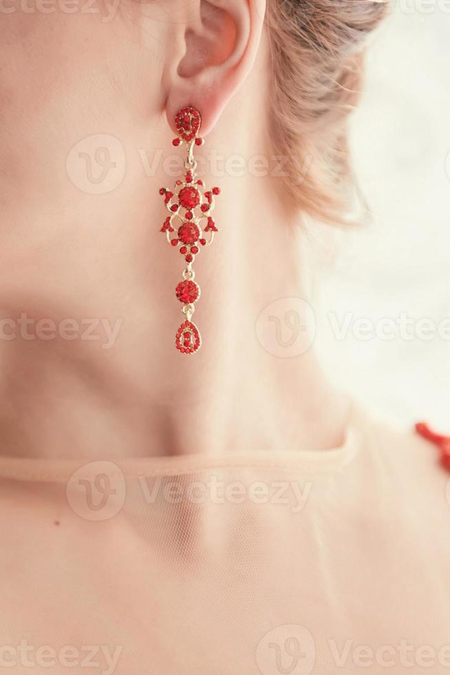 damesoorbellen met stenen, sieraden, oorbellen aan het oor van een mooi meisje, damesaccessoires, gouden oorbellen, oorbellen met rode stenen foto