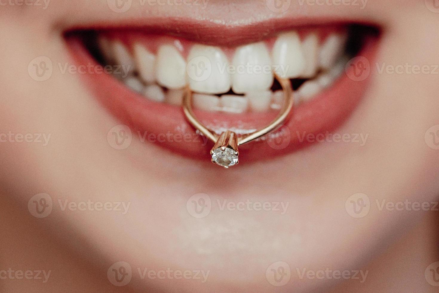 close-up jonge bruid toont haar trouwring houden in tanden en glimlachen. vrouw met diamanten ring en rode lippen. foto