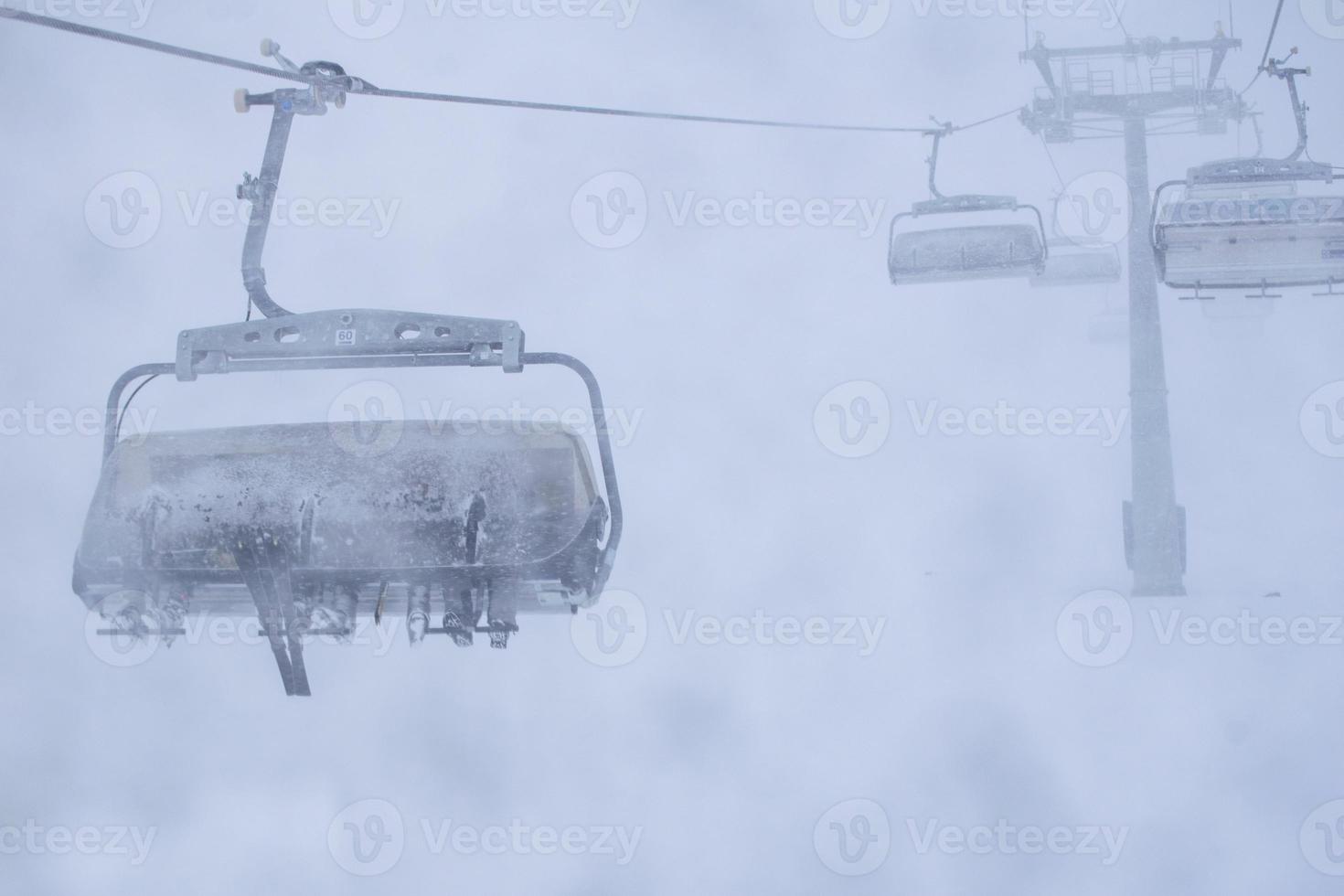 drie personen in ski's zitten op de stoeltjeslift van het skioord in stormachtige winterse omstandigheden. slecht zicht en weer in het concept van het skigebied. foto