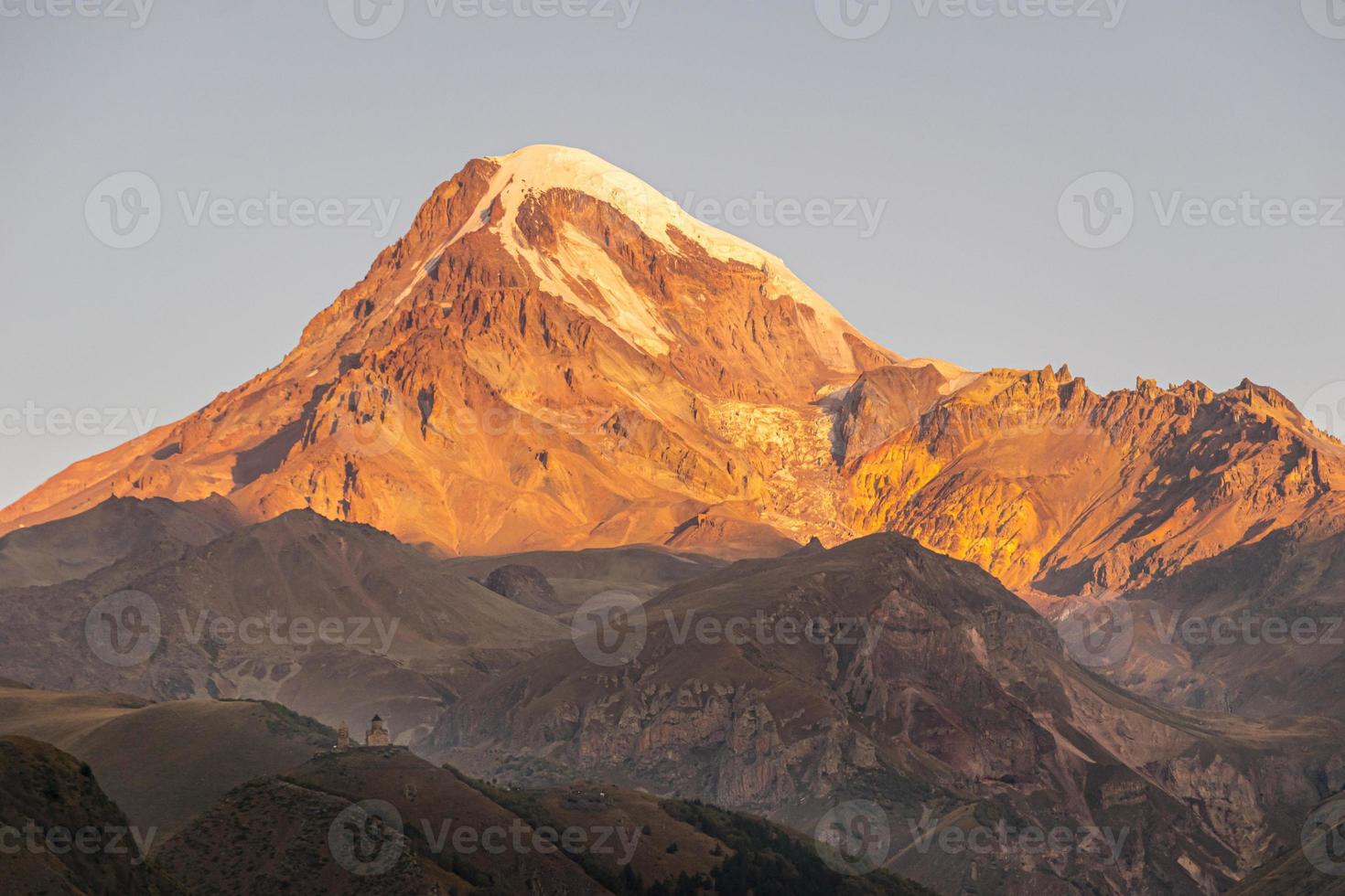 prachtig schilderachtig uitzicht op de bergtop van Kazbek tijdens zonsopgang en de Gergeti-kerk op de voorgrond foto