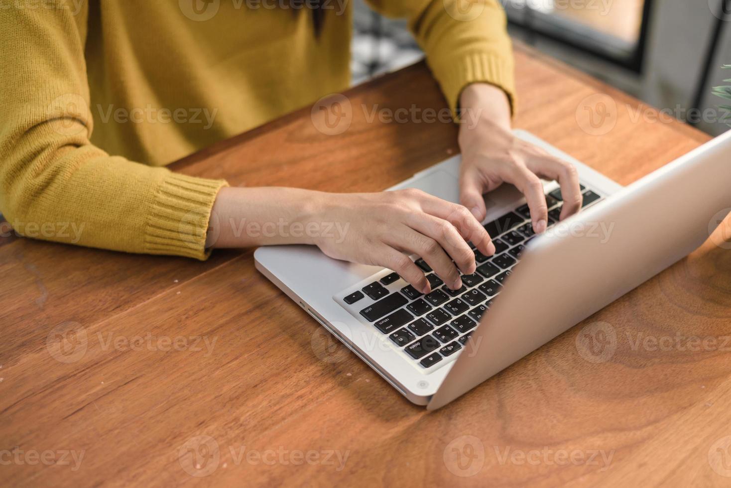 close-up van een jonge vrouw die met de laptop op een bureau in de coffeeshop werkt. jonge vrouw die in het weekend met haar laptop werkt in een warme zonlichtdag. laptop die in het coffeeshopconcept werkt. foto