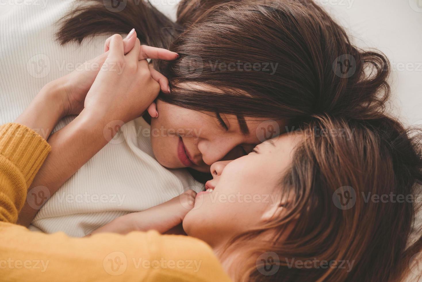 mooie jonge Aziatische vrouwen lgbt lesbische gelukkige paar knuffelen en glimlachen terwijl ze samen in bed onder deken thuis liggen. grappige vrouwen na het wakker worden. LGBT lesbisch koppel samen binnenshuis concept. foto