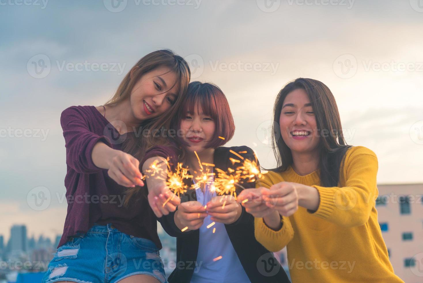 buitenopname van jonge mensen op een feestje op het dak. gelukkige groep aziatische vriendinnen geniet en speelt sterretje op het dakfeest bij avondzonsondergang. vakantie viering feestelijke partij. tiener levensstijl feest. foto