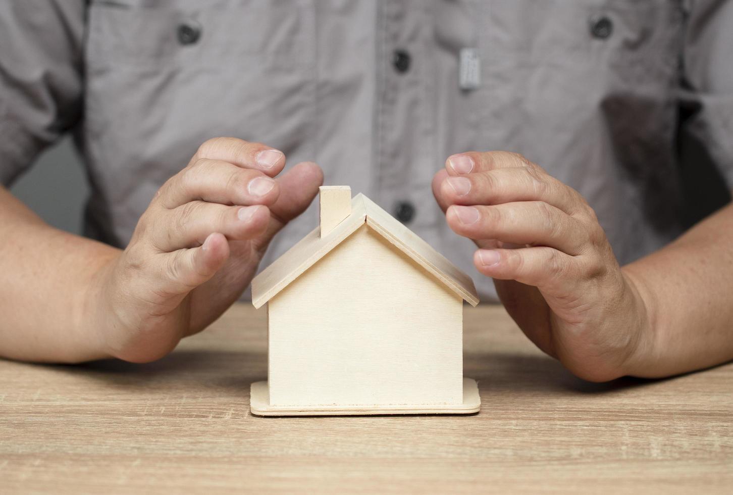 beschermingsconcept, liefde houden, mannelijke hand bewaakt houten huis op bruine tafel foto