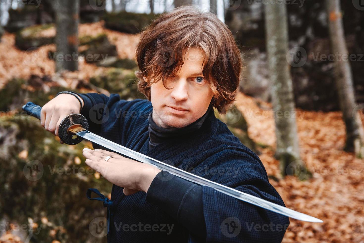 man in kimono die vechtsporten beoefent met een zwaard op rotsen en bosachtergrond foto