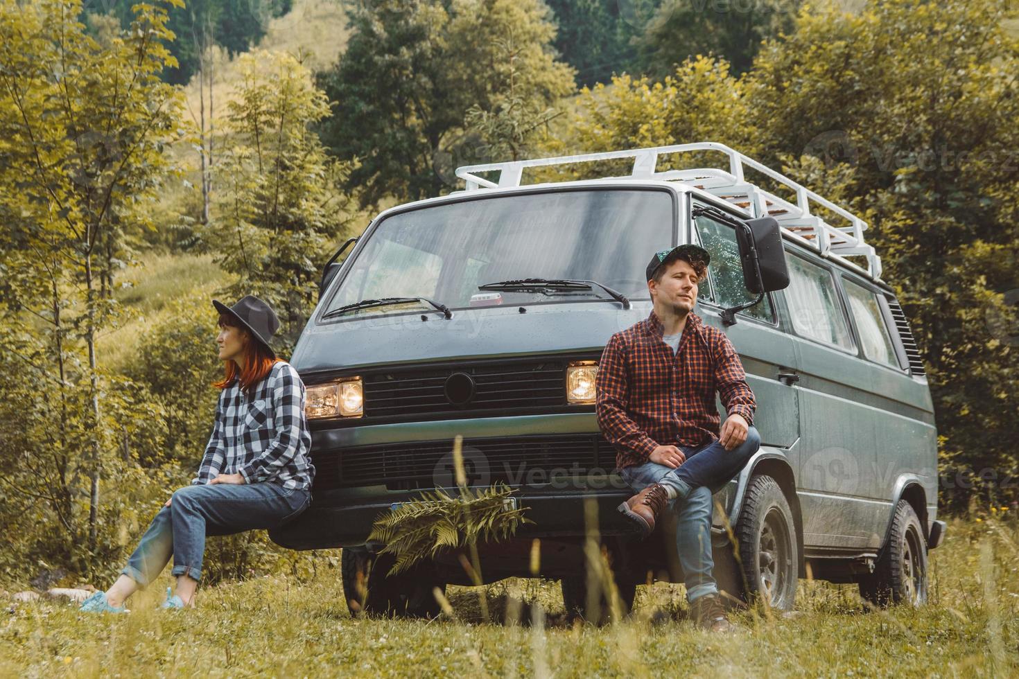 man en vrouw zitten in de buurt van busje op bergen en bos achtergrond foto