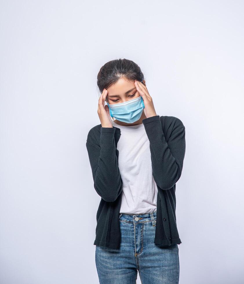 een zieke vrouw met hoofdpijn droeg een masker en legde een hand op haar hoofd. foto