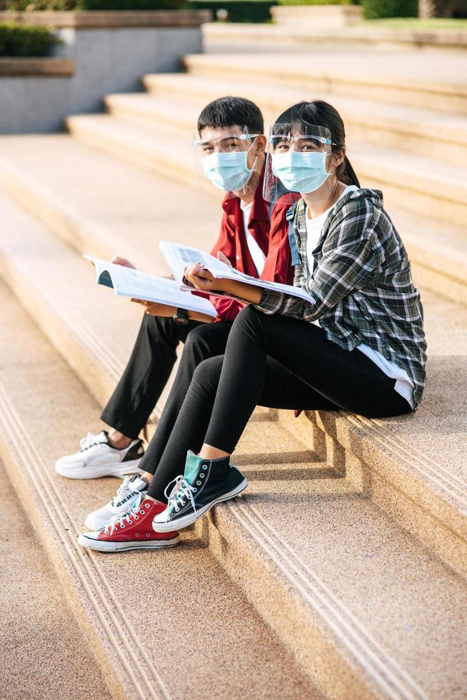 mannelijke en vrouwelijke studenten met maskers zitten en lezen boeken op de trap foto