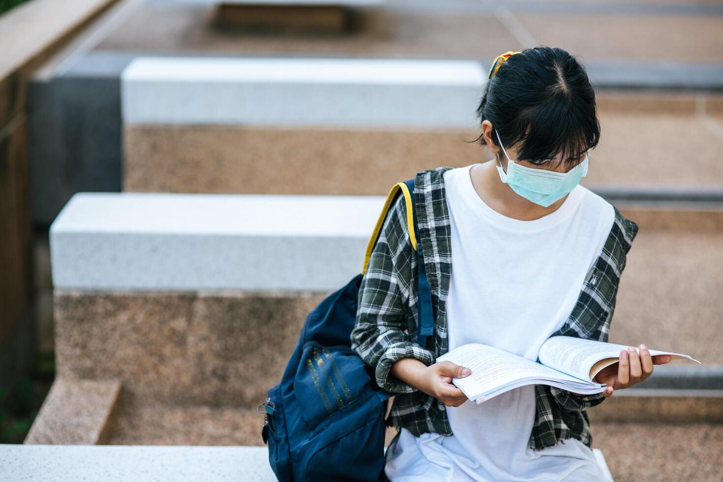 vrouwelijke studenten met maskers en boeken op de trap. foto