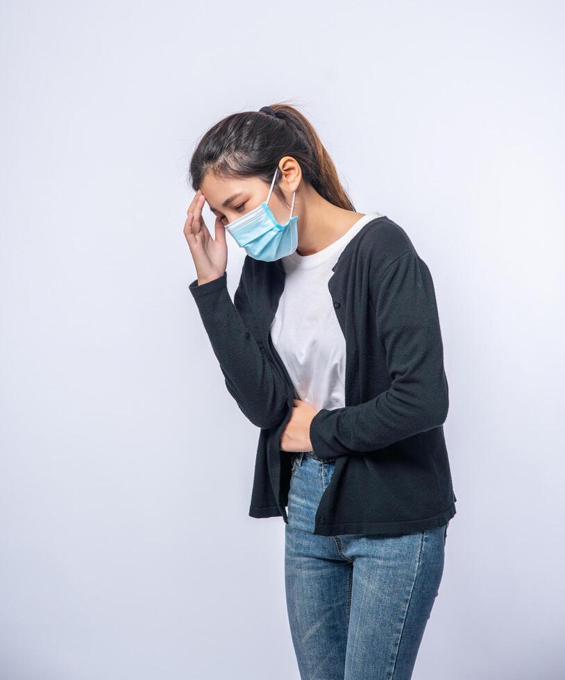 een zieke vrouw met hoofdpijn droeg een masker en legde een hand op haar hoofd. foto