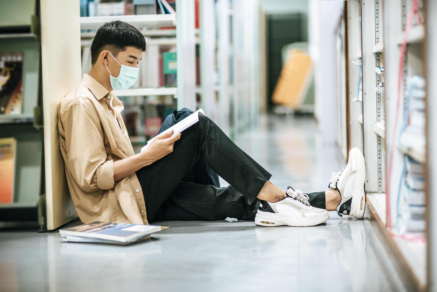 een man met maskers zit een boek te lezen in de bibliotheek. foto