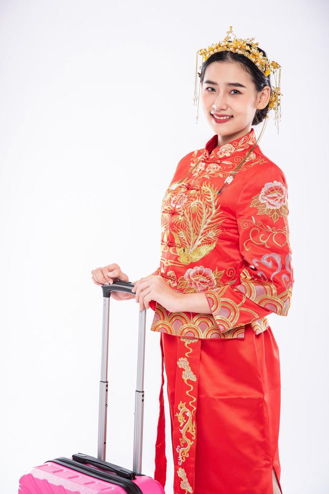 vrouw draagt cheongsam-pak met kroon bereid roze reistas voor op reis in chinees nieuwjaar foto