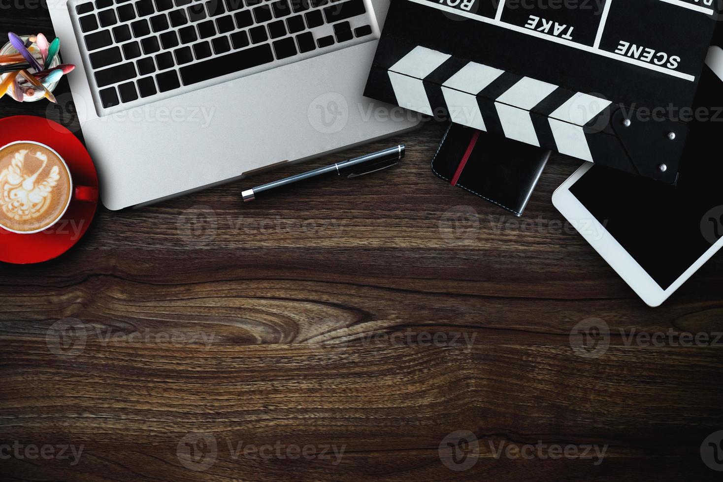 kantoorspullen met filmklep, laptop, smartphone, tablet, koffiekopje, pen, notitieblok en documenten op het houten tafelblad. foto