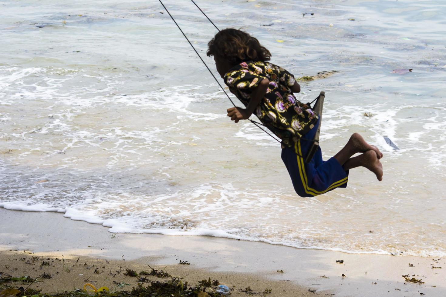 sorong, west papua, indonesië, 12 december 2021. een jong meisje aan het schommelen aan de rand van het strand foto