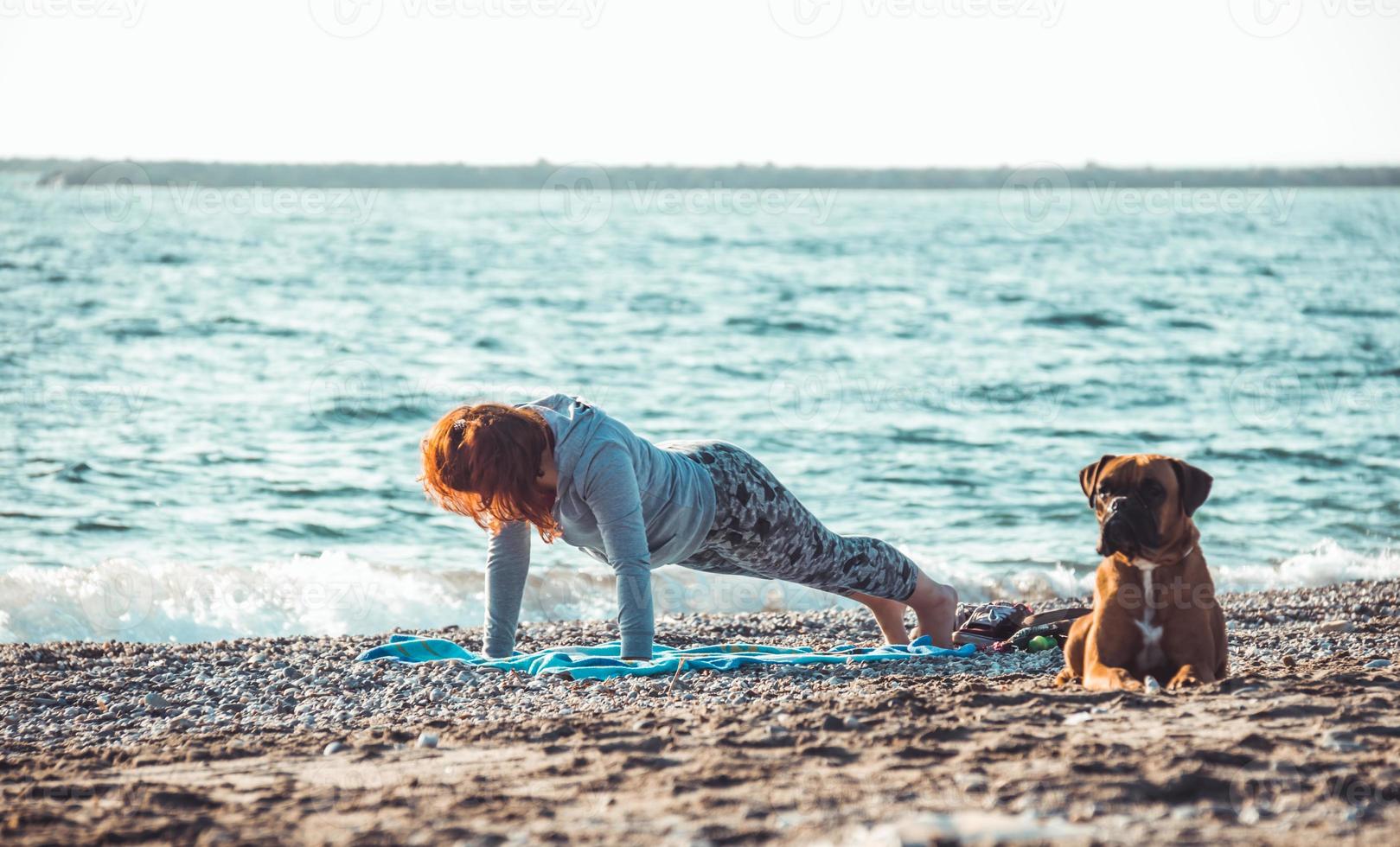 meisje doet yoga en strekt zich uit op het strand met haar hond foto