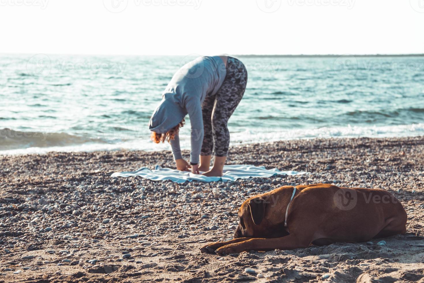 meisje doet yoga en strekt zich uit op het strand met haar hond foto