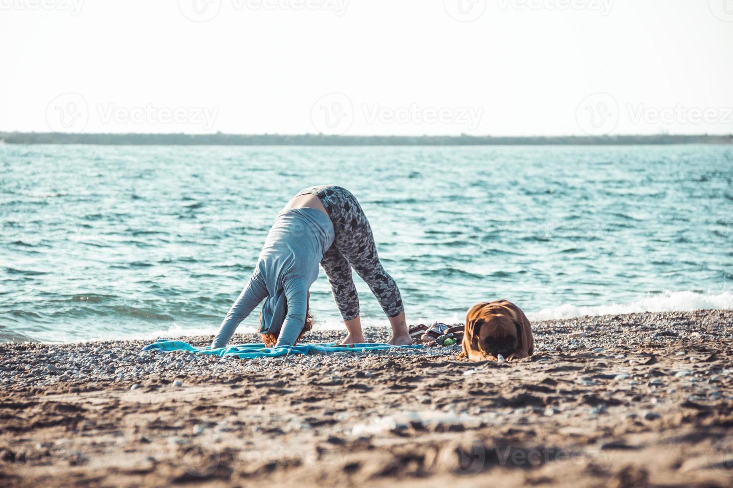 jonge vrouw doet yoga en strekt zich uit op het strand met haar hond foto